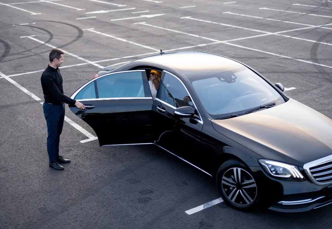 Chauffeur tenant la porte d'une voiture à une passagère qui sort